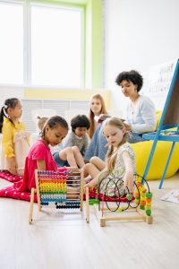 The mental health and physical health benefits of Montessori learning shown in a mixed age class. Many children with two using an abacus.